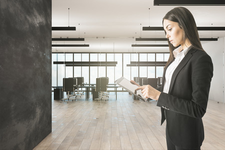 Attractive businesswoman using tablet in modern office with panpramic city view. Technology and communication concept.の写真素材
