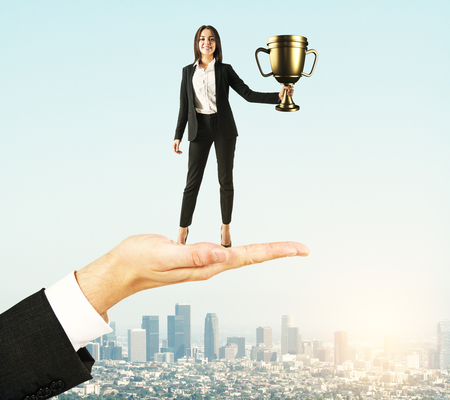 Hand holding businesswoman with golden cup on sky background. Leadership and success conceptの写真素材