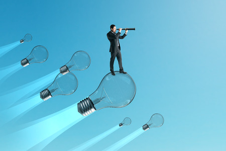 Businessman looking into thr distance on while flying on lamps on blue sky background. Idea and research concept.の写真素材