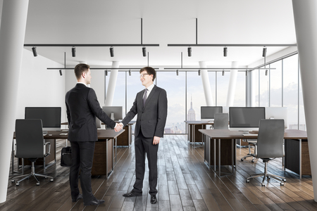 Attractive european businessmen shaking hands in modern office interior with city view and daylight. Teamwork and deal concept.の写真素材