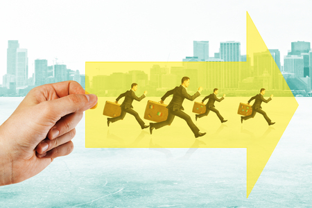 Hand holding arrow with running businessmen on city background. Growth, teamwork and competitor conceptの写真素材