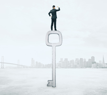 Young businessman standing on abstract key on city background. Access and research conceptの写真素材