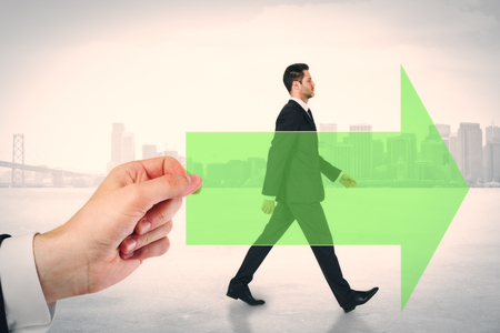 Hand holding green arrow with walking european businessman on city background. Growth and development conceptの写真素材