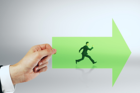 Hand holding green arrow with running businessman on grey background. Growth and success conceptの写真素材