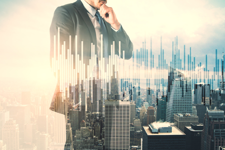 Attractive young european businessman thinking on city background with forex chart. Trade and finance concept. Double exposureの写真素材