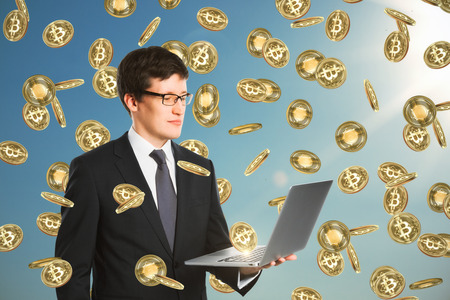 Businessman with laptop celebrating golden bitcoin rain on sky background. Cryptocurrency and finance conceptの写真素材