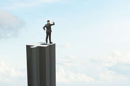 Businessman looking into the distance from jigsaw skyscraper on sky background with clouds. Vision and research concept.の写真素材