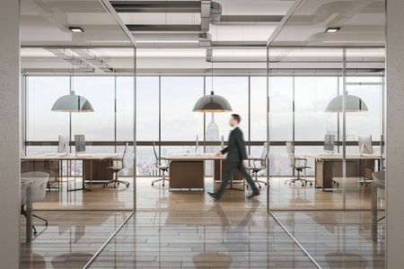 Side view of young businessman walking in contemporary office interior with city view. Workplace concept.の写真素材