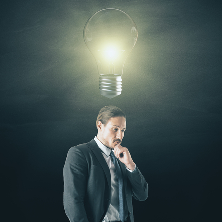 Portrait of attractive young businessman with lamp on dark background. Idea and solution conceptの写真素材