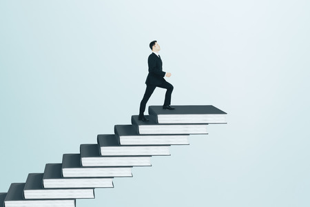 Businessman climbing book pile ladder. Sky background. Education and growth conceptの写真素材