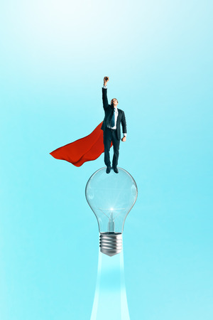 Superhero businessman flying with launching lamp on blue background. Confidence and success conceptの写真素材