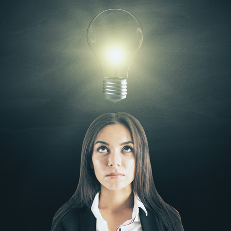Portrait of attractive young businesswoman with lamp on dark background. Idea and solution conceptの写真素材