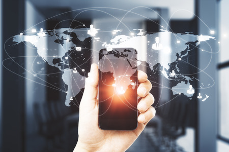 Hand holding smartphone with digital map on blurry office interior background. Communication and network concept. Double exposureの写真素材