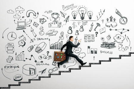 Side view of young businessman with travel briefcase running up drawn stairs on concrete wall with creative business sketch. Success and marketing conceptの写真素材