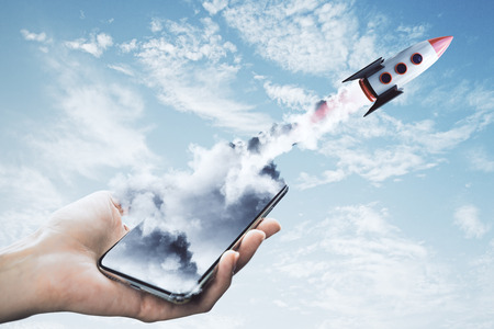 Hand holding smartphone with launching rocket on sky background. Startup and web conceptの写真素材