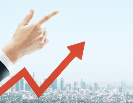 Businessman hand and red arrow pointing up on blurry sky and city background with copy space. Up and...