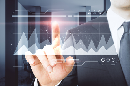 Businessman hand pointing at glowing business chart in blurry office interior. Innovation and financial growth concept.の写真素材