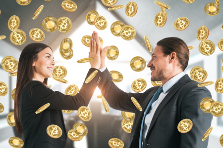 Happy european businessman and woman hi-fiving each other in blurry office interior with bitcoin rain. Success and cryptocurrency concept.の写真素材