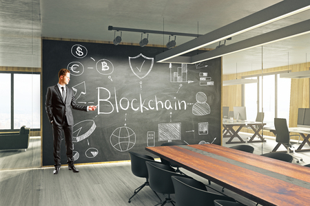 Attractive young businessman drawing blockchain sketch in modern meeting room interior. Cryptocurrency and cyber concept.の写真素材