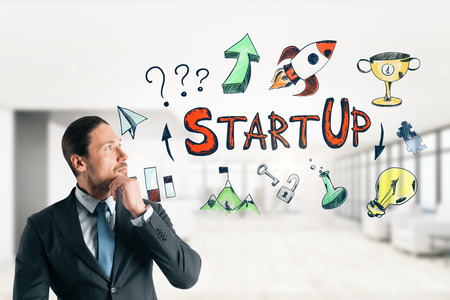 Attractive young european businessman drawing startup sketch in modern white office interior. Start up and finance conceptの写真素材
