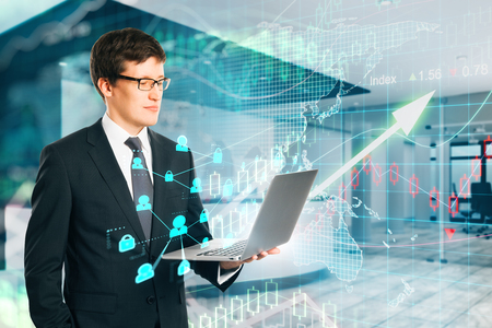 Attractive young businessman using laptop in blurry office with increasing forex chart arrow. Investment and finance concept. Double exposureの写真素材