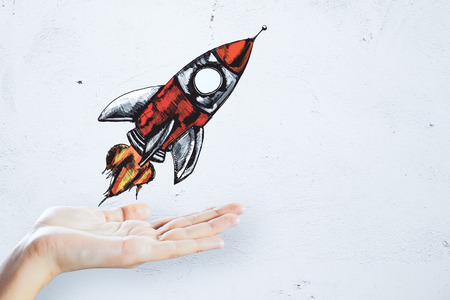Hand holding creative rocket sketch on concrete wall background. Startup and project conceptの写真素材