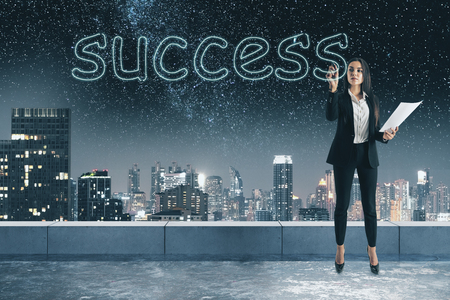 Young businesswoman writing abstract success word on concrete rooftop background with blurry night city view. Successful female conceptの写真素材