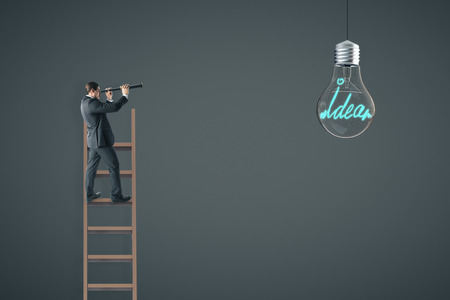 Businessman on ladder using telescope to look at hanging light bulb. Dark wall background. Idea and innovation conceptの写真素材
