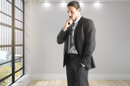 Thinking businessman standing in modern office interior. Worker and executive concept.の写真素材