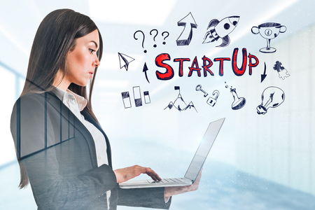 Attractive young businesswoman using laptop in modern blurry office interior with startup sketch. Start up and success concept. Double exposureの写真素材