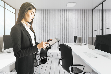 Attractive young european businesswoman using tablet in modern white office interior. Technology and communication concept.の写真素材