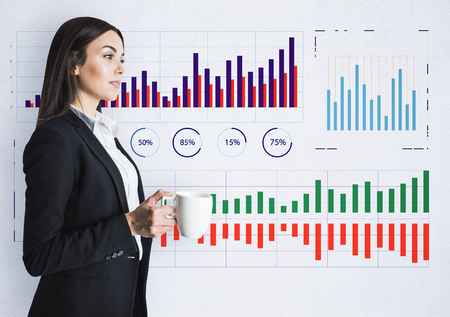 Attractive young businesswoman with coffee cup standing on concrete wall background with business charts sketch. Finance and money conceptの写真素材