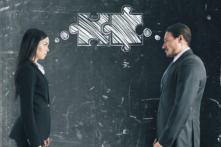 Attractive young businessman with female colleague thinking about puzzles pieces on grunge concrete wall background. Teamwork and join conceptの写真素材