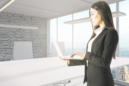 Pretty young businesswoman using laptop in modern office interior. Technology and communication concept.の写真素材