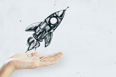 Hand holding creative rocket sketch on concrete wall background. Startup and business conceptの写真素材