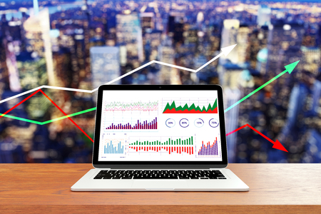 Close up of laptop with business charts on wooden desk and blurry night city background with arrows. Economy and technology concept. 3D Renderingの写真素材
