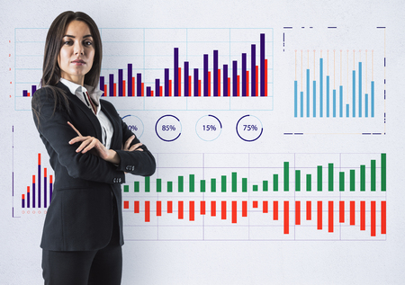 Attractive young businesswoman standing on concrete wall background with business charts sketch. Finance and economy conceptの写真素材