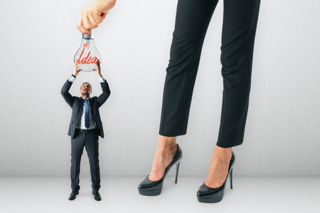 Businesswoman hanging lamp to tiny businessman on concrete background. Teamwork and innovation concept