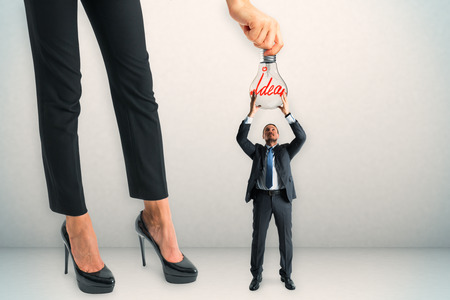 Businesswoman hanging lamp to tiny businessman on concrete background. Teamwork and invention conceptの写真素材