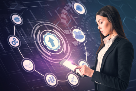Side view of attractive young businesswoman using tablet on blue background with abstract business interface. Technology and network concept.の写真素材