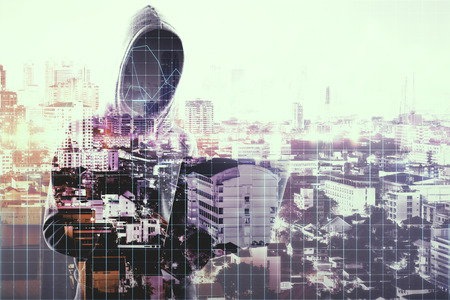 Hacker with laptop standing on abstract city background. Hacking and finance concept. Double exposureの写真素材