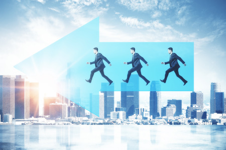 Side view of young businessmen running on blue arrow on city background with sunlight. Success and teamwork conceptの写真素材