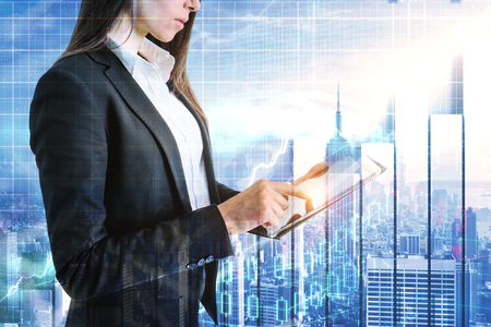 Side view of attractive young businesswoman using laptop on abstract New York city background with forex chart. Broker and trade concept. Double exposureの写真素材