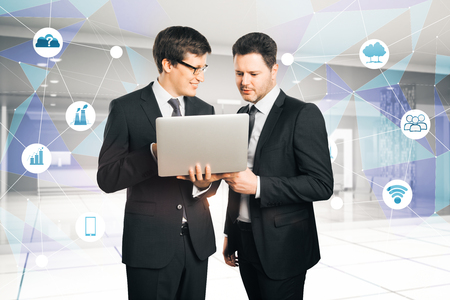 Businessmen using laptop in modern office interior with business hologram. Teamwork and finance concept. Double exposureの写真素材
