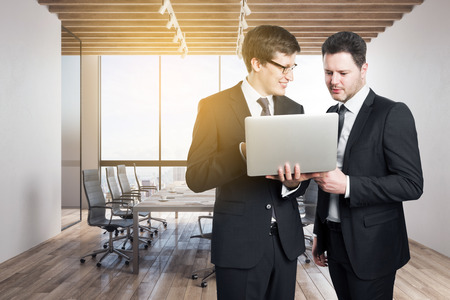 Attractive european businessmen using laptop in modern meeting room interior with sunlight, city view and furniture. Teamwork and communication concept.の写真素材