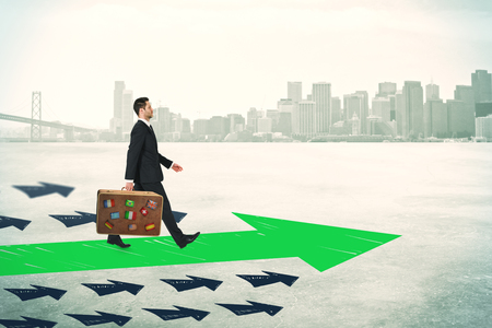 Side view of young businessman with travel briefcase following drawn arrows on light city background. Success and way conceptの写真素材