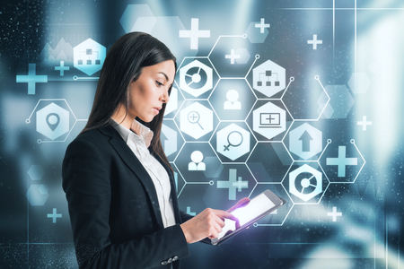 Attractive young businesswoman with tablet using creative medical interface on blurry background. Medicine and technology concept.の写真素材
