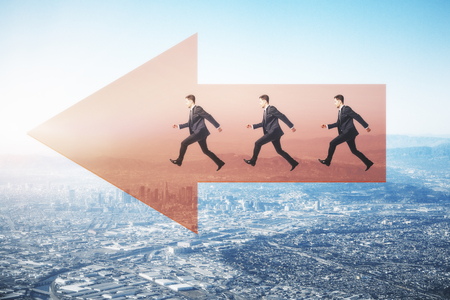 Side view of young businessmen running on red arrow on city background with daylight. Direction and teamwork conceptの写真素材