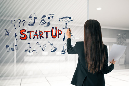 Back view of attractive young european businesswoman drawing start up sketch in modern office reception interior. Startup and workshop concept.の写真素材