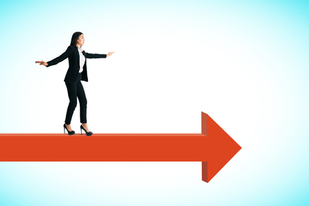 Side view of attractive young european businesswoman balancing on red arrow. Sky background. Challenge and way conceptの写真素材